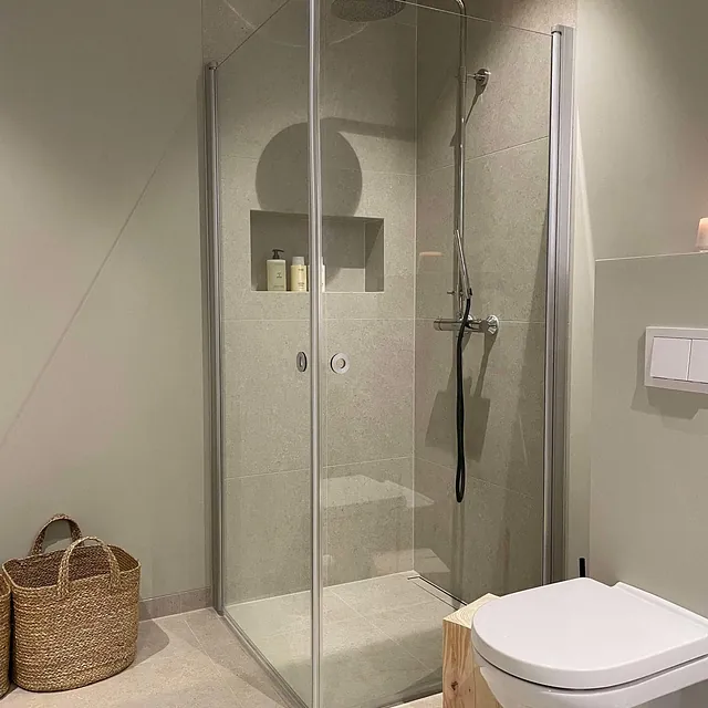 Stilrent bad med dusjhjørne, vegghengt toalett og integrert nisje for oppbevaring.