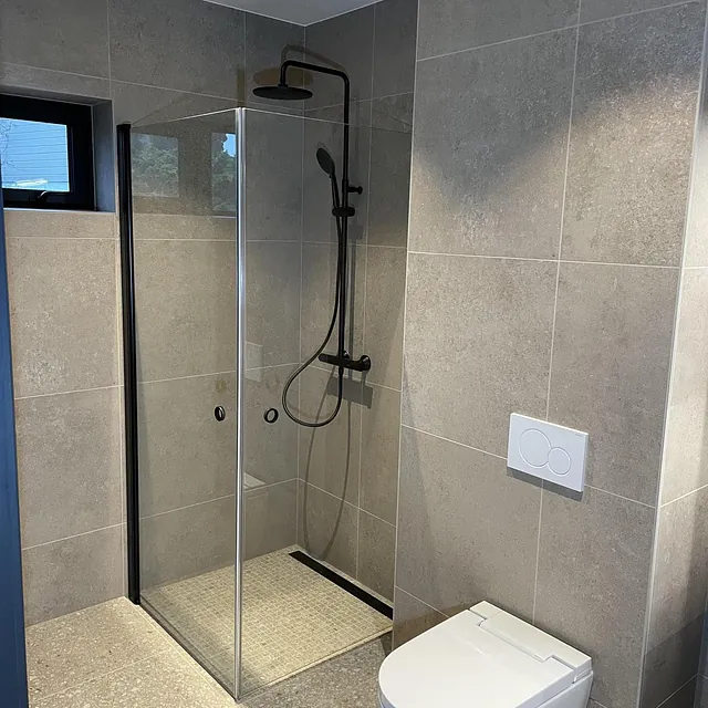 Moderne bad med dusjhjørne, vegghengt toalett og flislagte overflater i nøytrale toner.