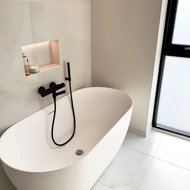 Lyst bad med frittstående badekar, sorte armaturer og nisjehylle i veggen.