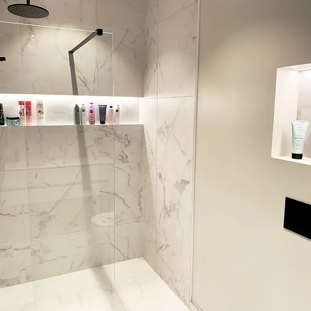Dusjsone med marmorfliser, sorte detaljer og innebygde hyller med belysning.