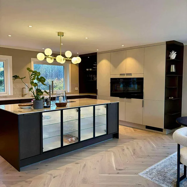 Moderne kjøkken med kjøkkenøy, integrerte hvitevarer og stilren belysning i åpen løsning.