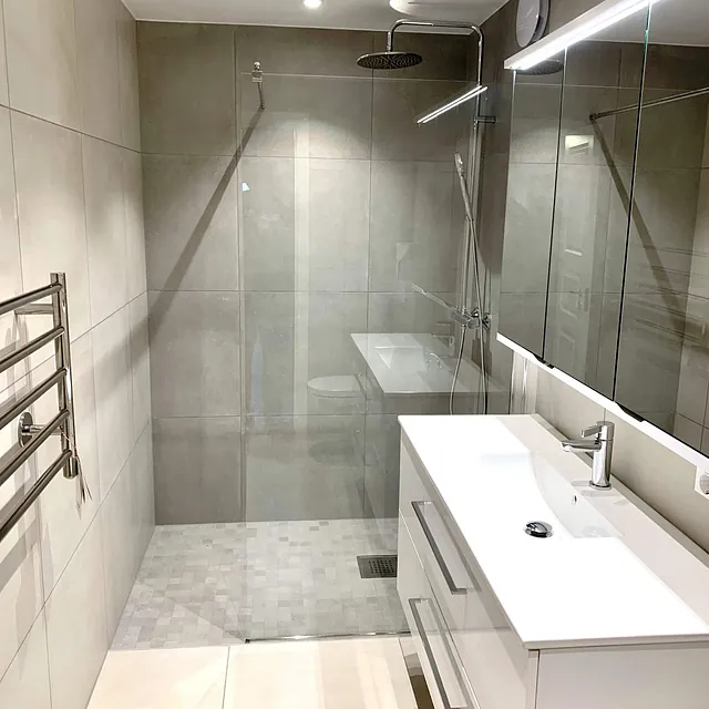 Moderne bad med stor dusjsone, glassvegger og hvit servantinnredning.