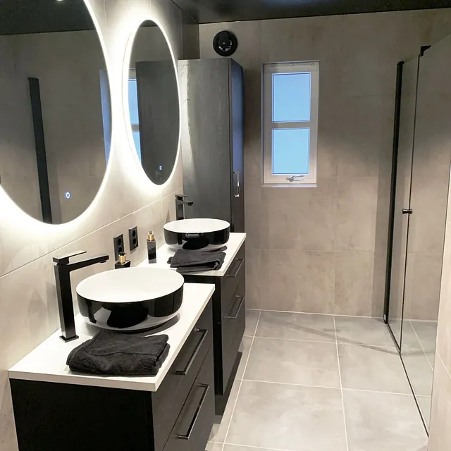 Bad med doble svarte servanter, runde speil og mørke møbler.