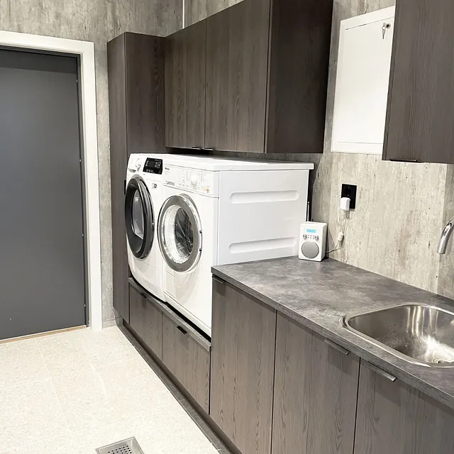 Vaskerom med mørke skap, vaskemaskin, tørketrommel og stålvask.