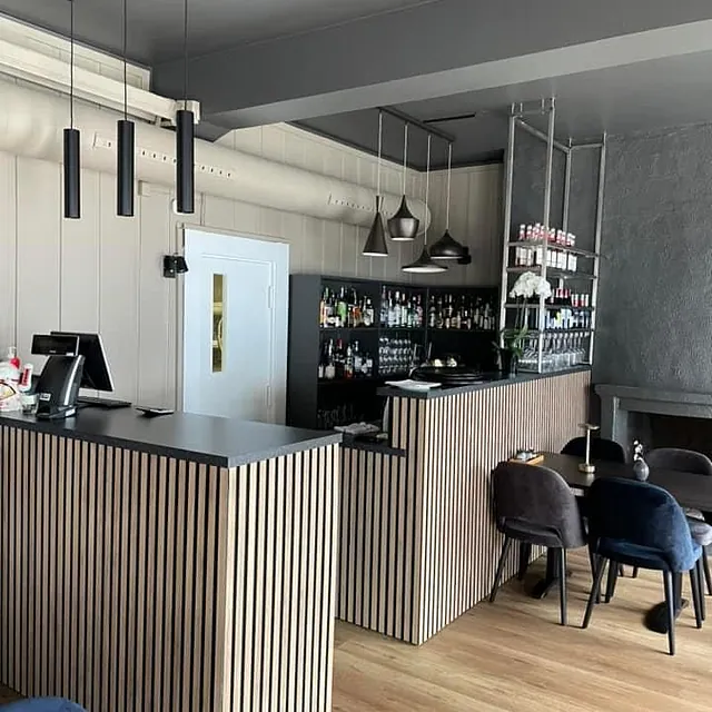 Barområde med striper i trepanel, svarte benkeplater og hyller med flasker.