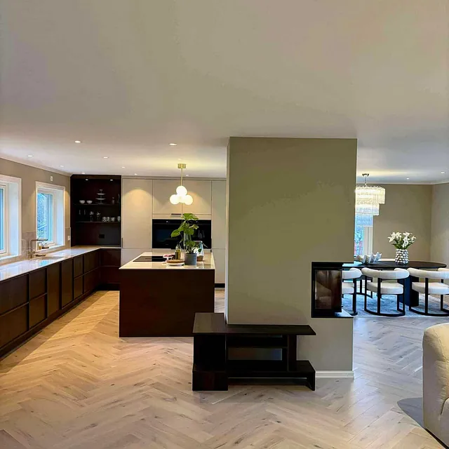 Åpen stue og kjøkkenløsning med parkettgulv, peis og spiseplass i moderne bolig.