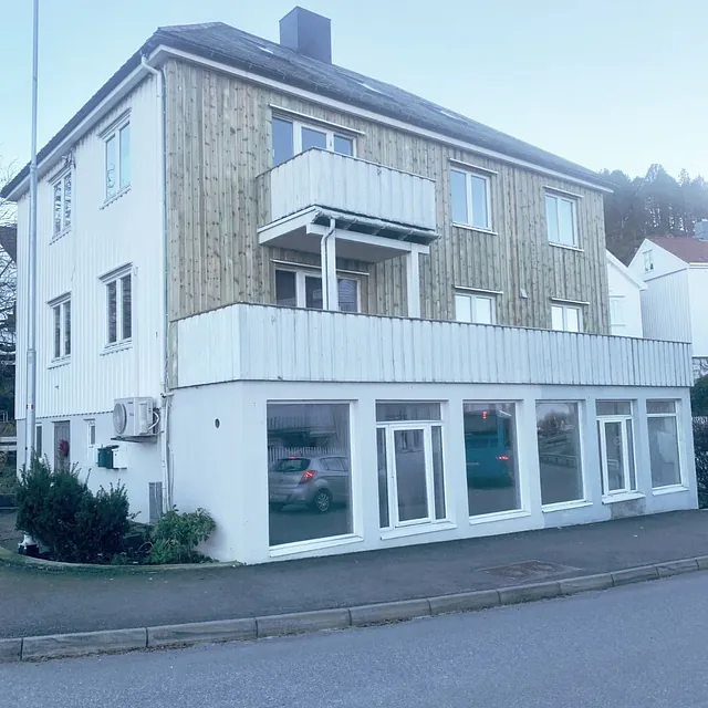Toetasjes bygg med hvit og trepanel fasade, store vinduer i første etasje.