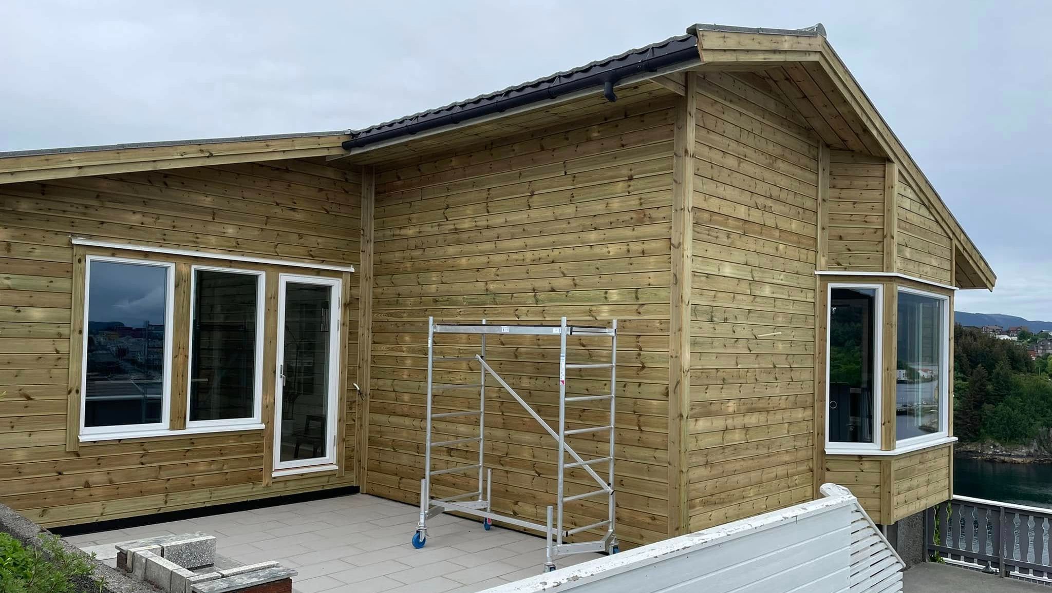 Hus med ny kledning i ubehandlet tre og stor terrasse foran vinduer.