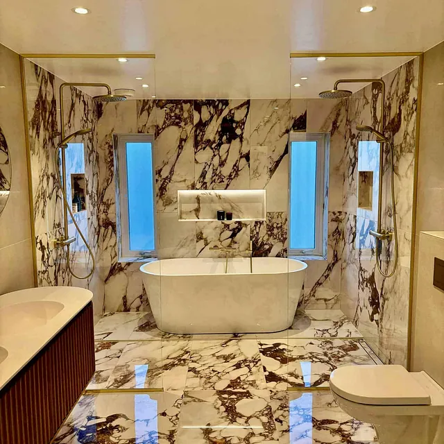 Eksklusivt bad med marmorfliser, frittstående badekar og dusj med glassvegger.