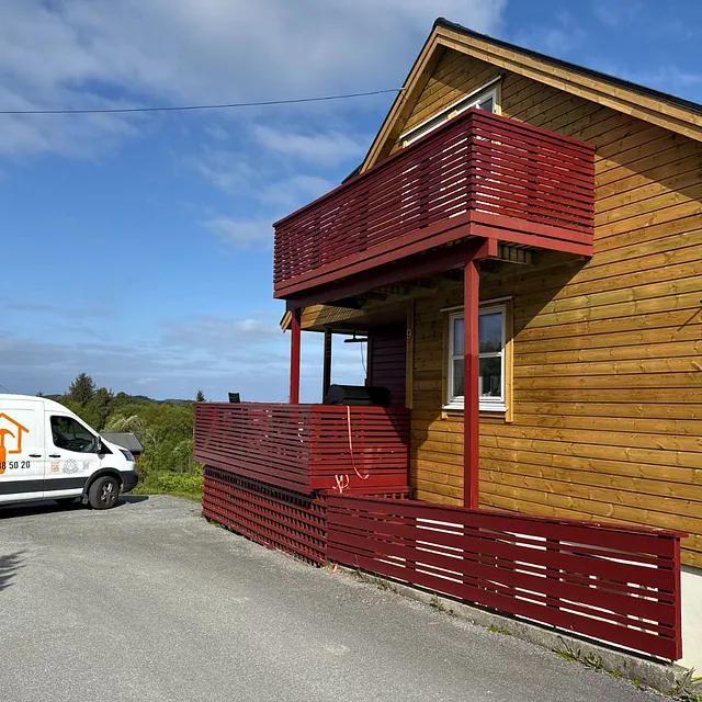 Hvit Byggeria-bil foran hus med nytt trepanel og rødmalt balkong.