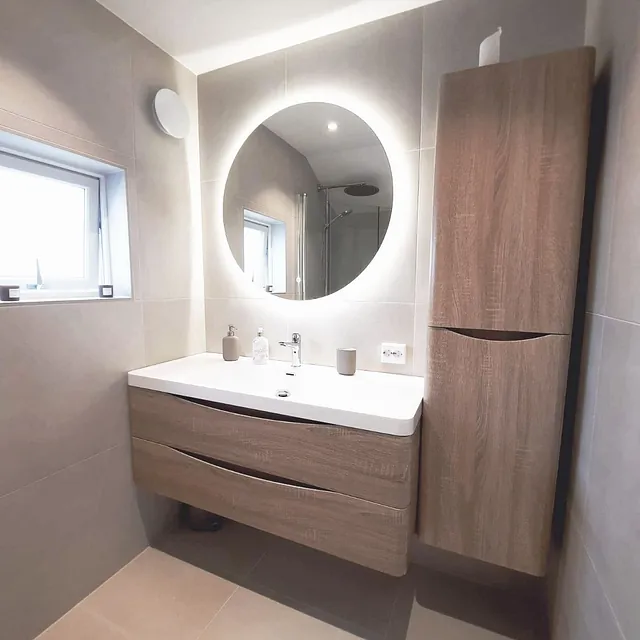 Bad med treinnredning, rundt speil med LED-lys og liten vindusåpning.